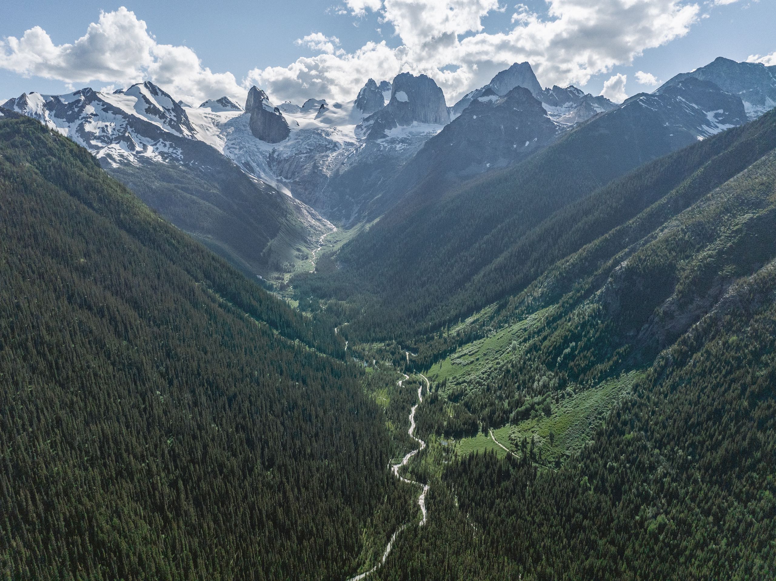An aerial view of the trees, mountain spires, and glacial turquoise waters in the Bugaboos mountain range, captured during a heli-hiking trip with CMH Bugaboos.