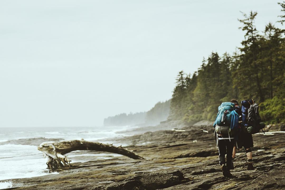 Hikers with large packs walk along the shoreline