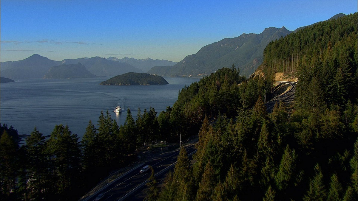Aerial view of a highway through trees next to a lake