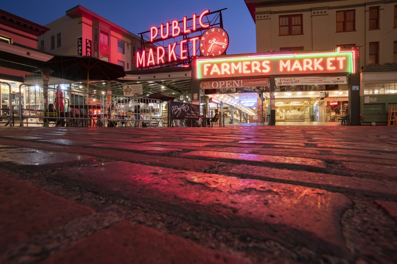 Neon signs light up the night sky, indicating a public market.