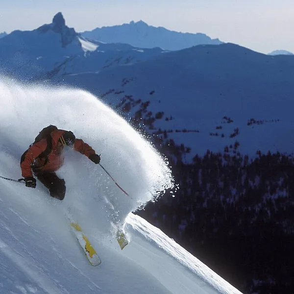 A skier does a powder slash at Whistler Blackcomb with the Back Tusk landmark in the background.