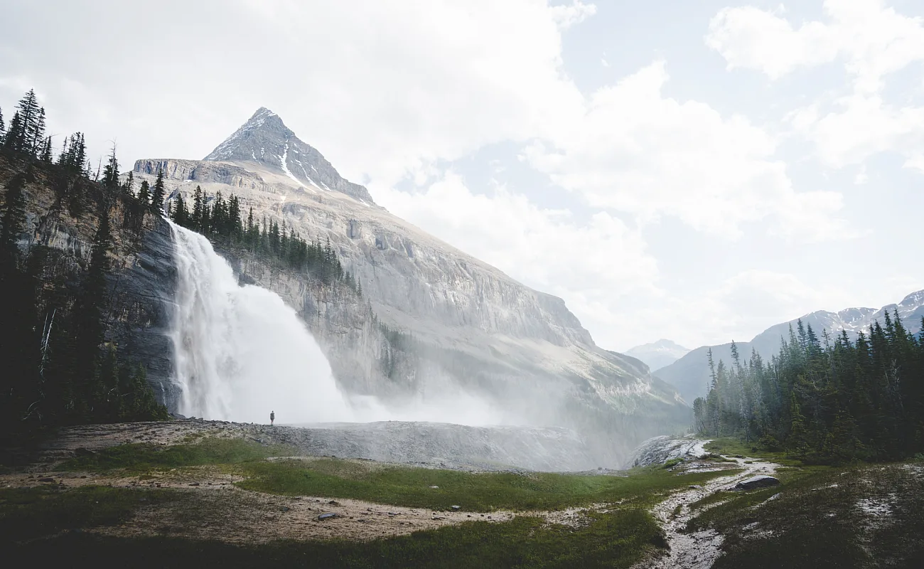 A figure is shown is hiking at Emperor Falls on the Berg Lake Trail in Mount Robson Provincial Park near Invermere, with cascading water in the background.