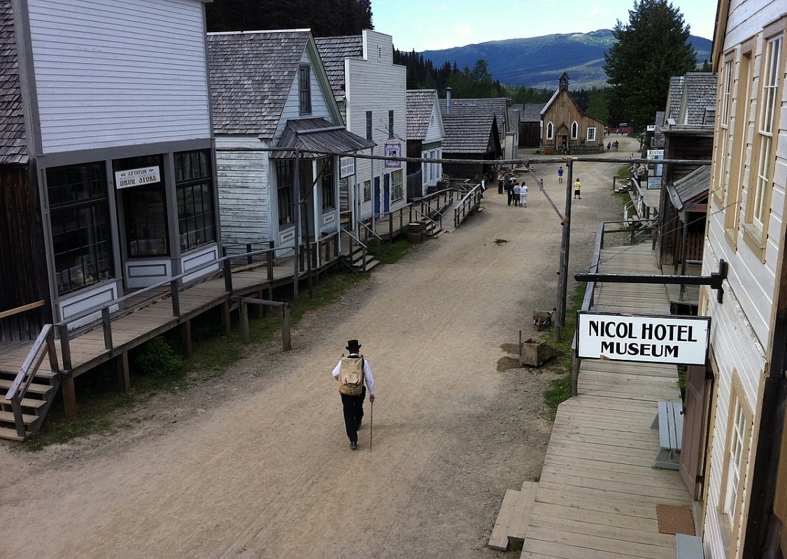 Un hombre con traje de época camina por una calle de edificios históricos en Barkerville Historic Town