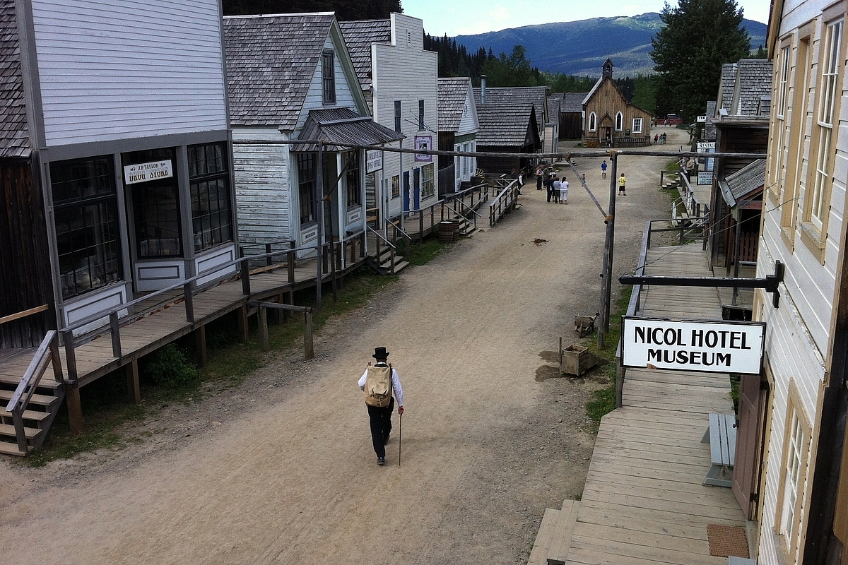 A man in period costume walks down a street of heritage buildings at Barkerville Historic Town