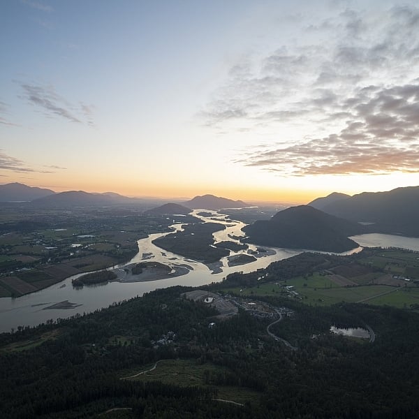 Una vista panorámica del Fraser River en un día despejado. Al fondo, se ven siluetas de montañas coronadas por el sol poniente.