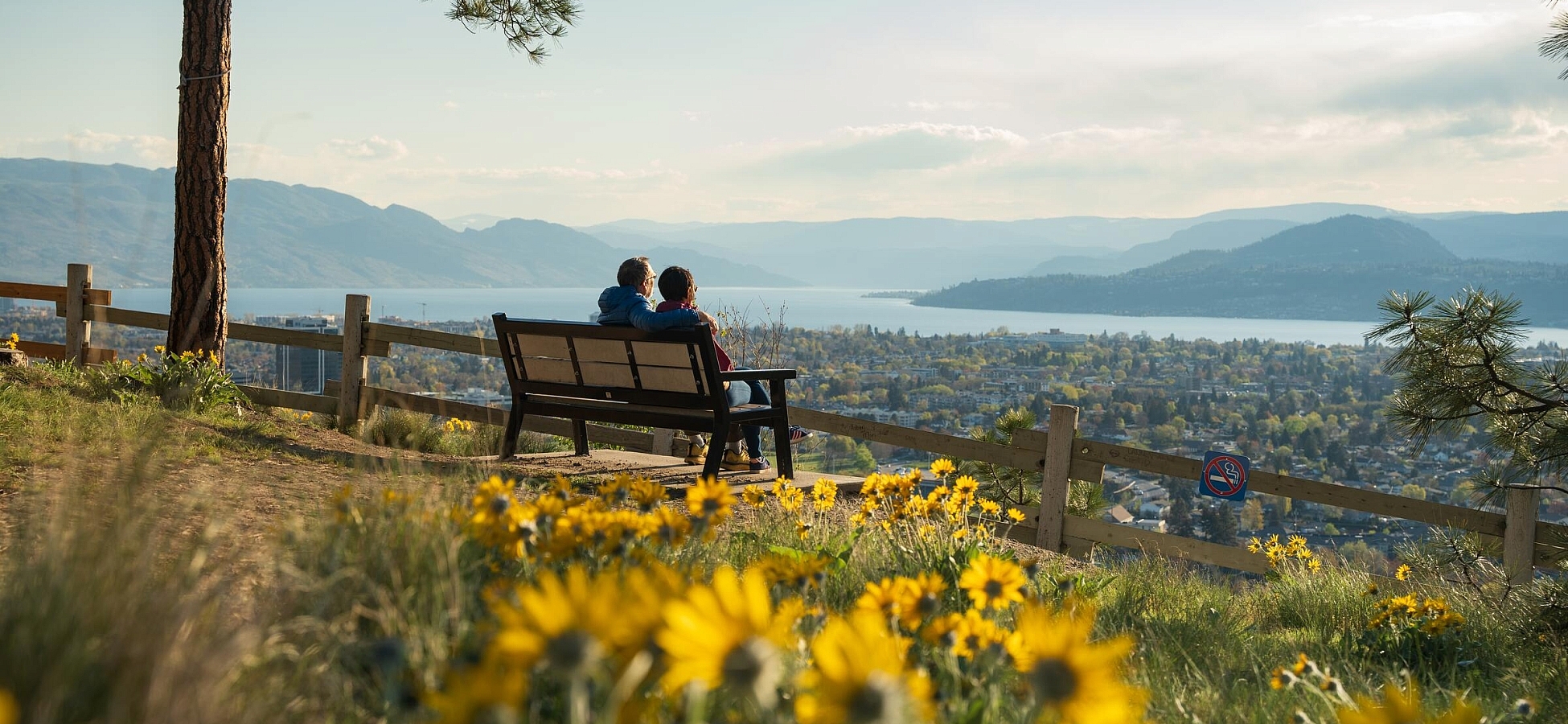 A couple sitting on a bench looking out at the view of Kelowna from Okanagan Lake.