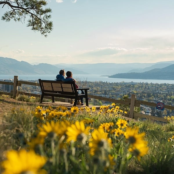 A couple sitting on a bench looking out at the view of Kelowna from Okanagan Lake.