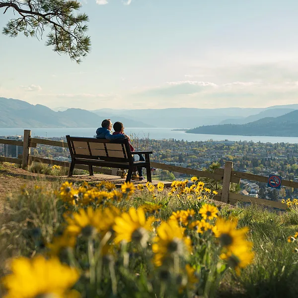 Una pareja sentada en una banca, contemplando la vista de Kelowna desde el lago Okanagan.