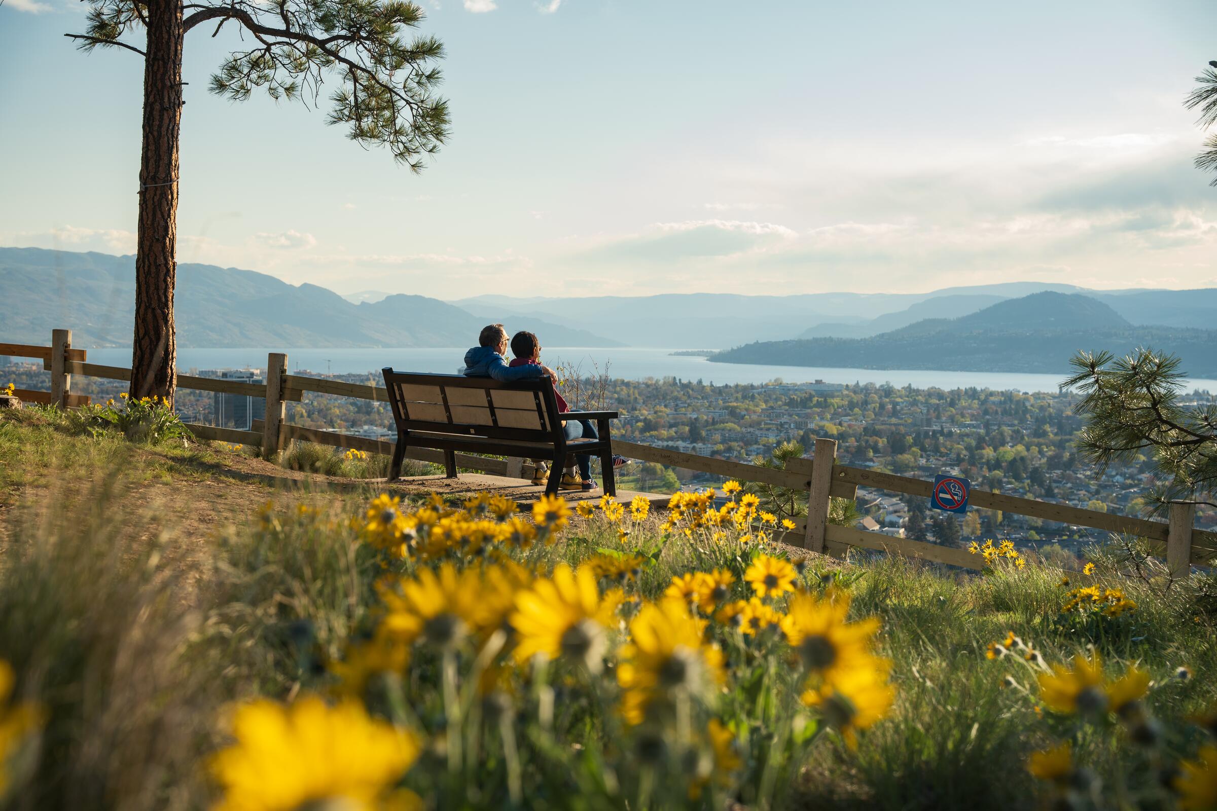 A couple sitting on a bench looking out at the view of Kelowna from Okanagan Lake.