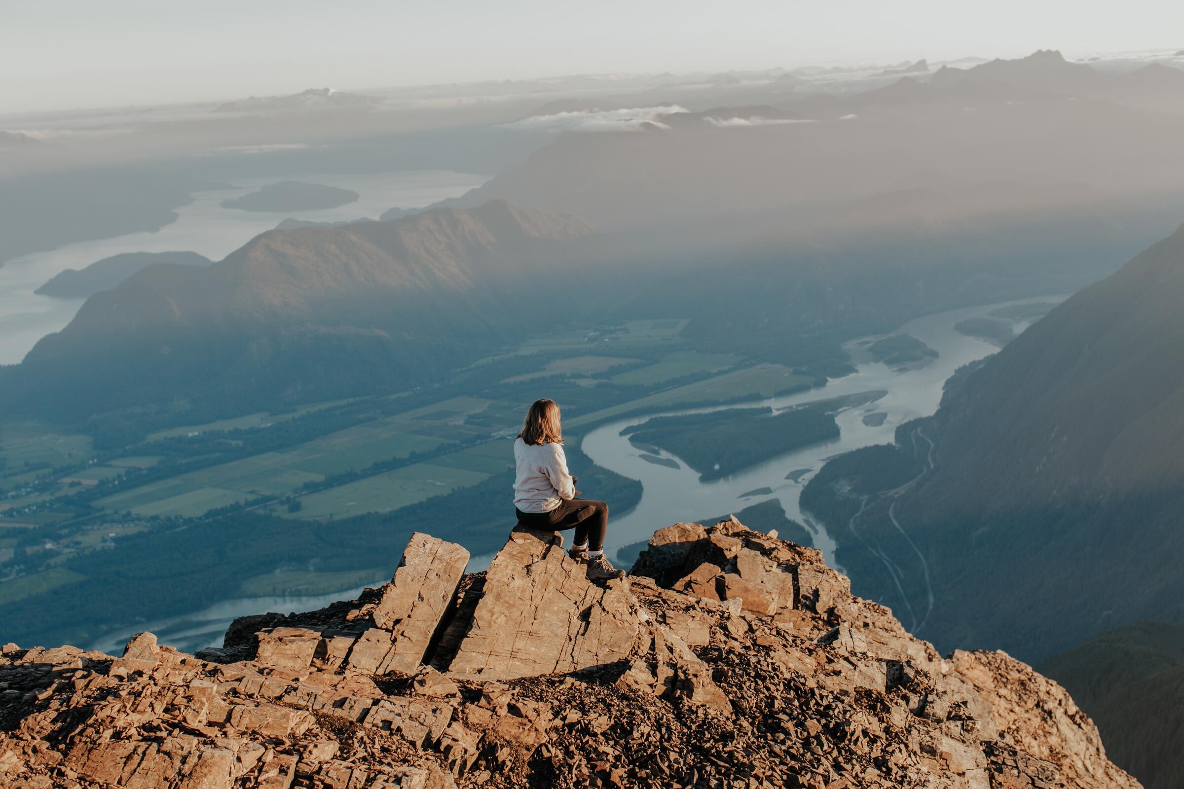 Hiker sitting on the rocks on top of Cheam Mountain looking out over the valley.