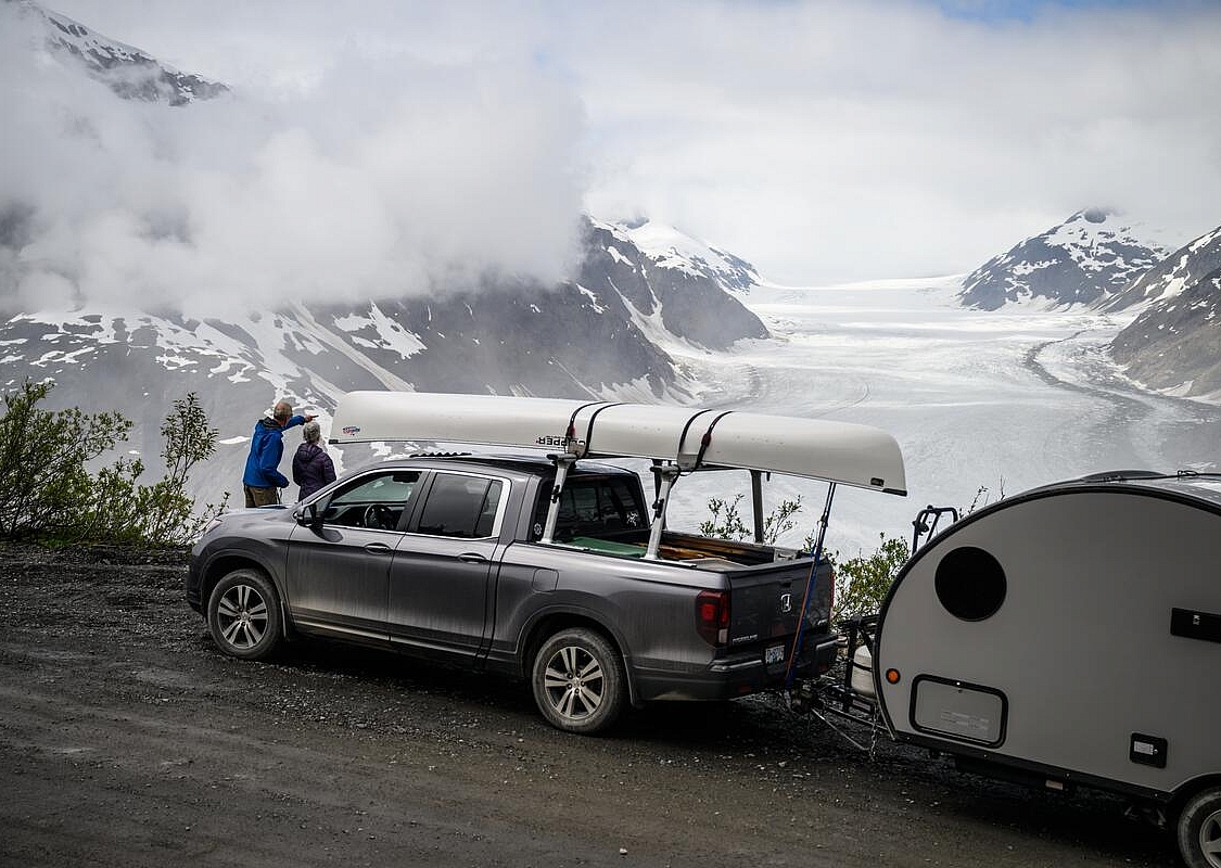 Ein Truck mit einem Kanu und einem kleinen Anhänger parkt am Aussichtspunkt mit Blick auf einen Gletscher.
