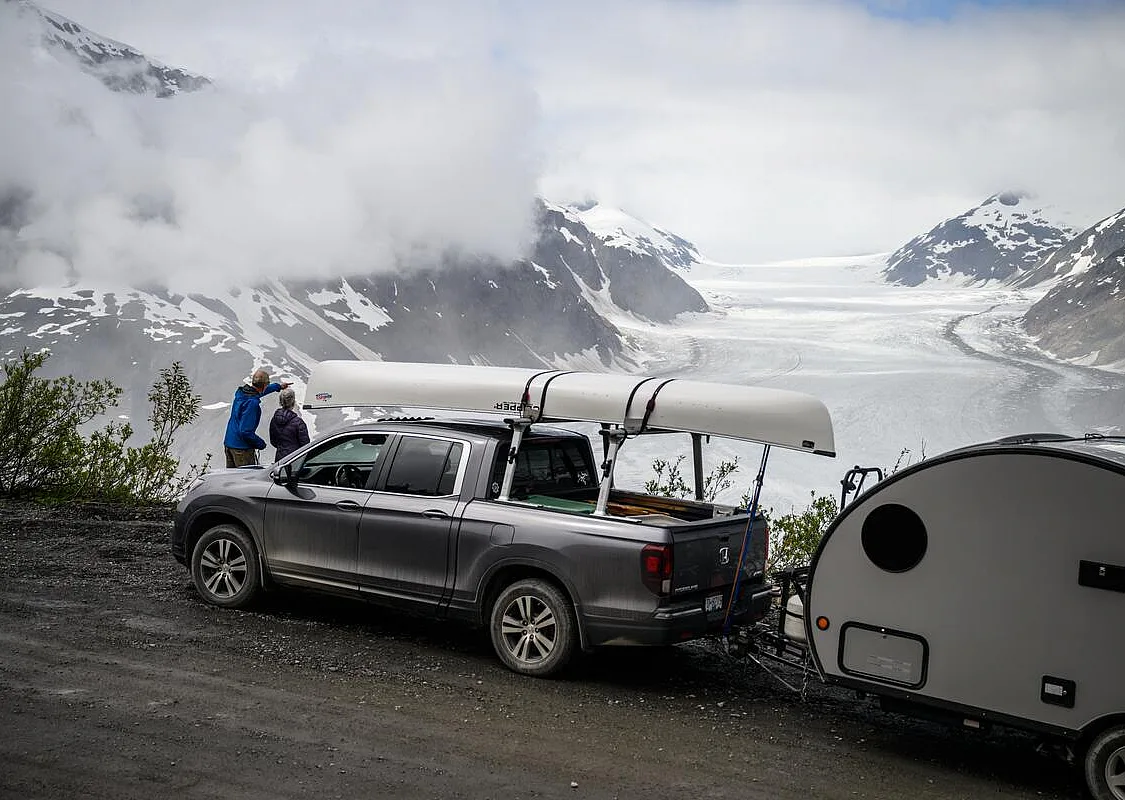 Truck carrying a canoe and pulling a small trailer parked at the viewing area overlooking a glacier.