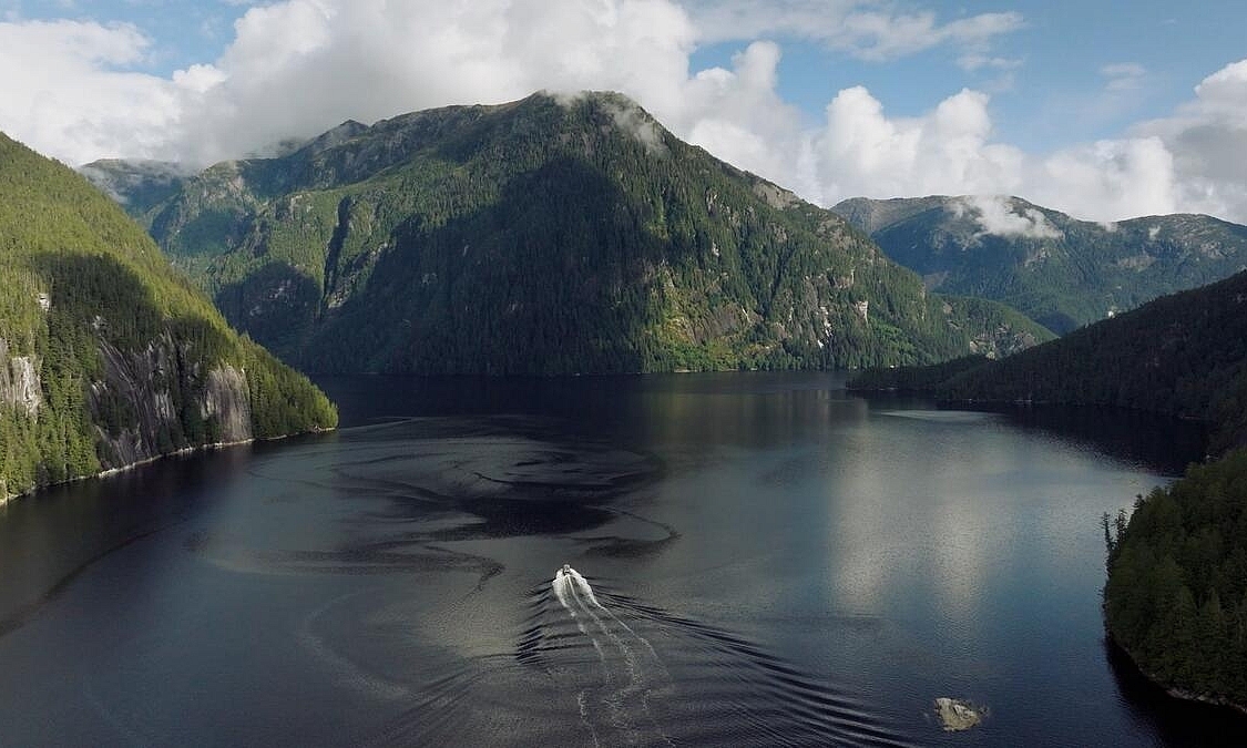 Luftaufnahme von bewaldeten Bergen, die aus dem Meer ragen, mit einem Boot, das auf das Land zusteuert.