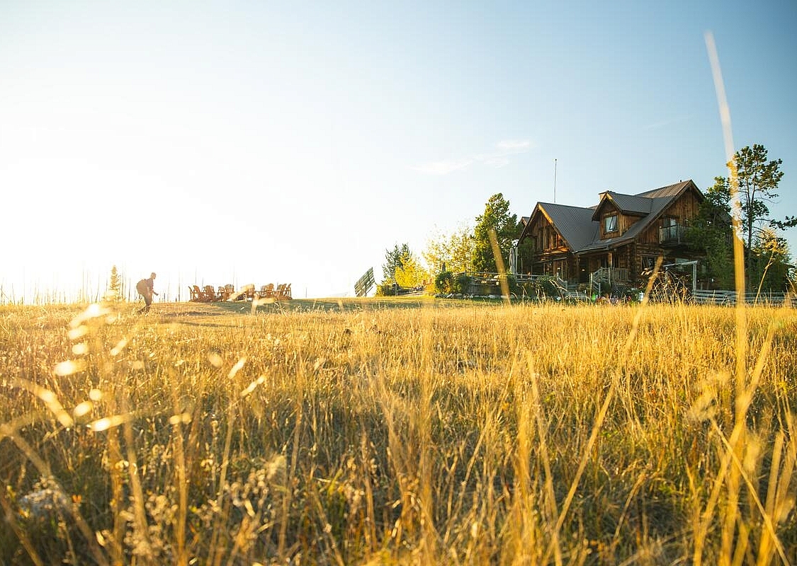 Ein*e Wander*in geht auf ein hölzernes Resortgebäude unter freiem Himmel zu.