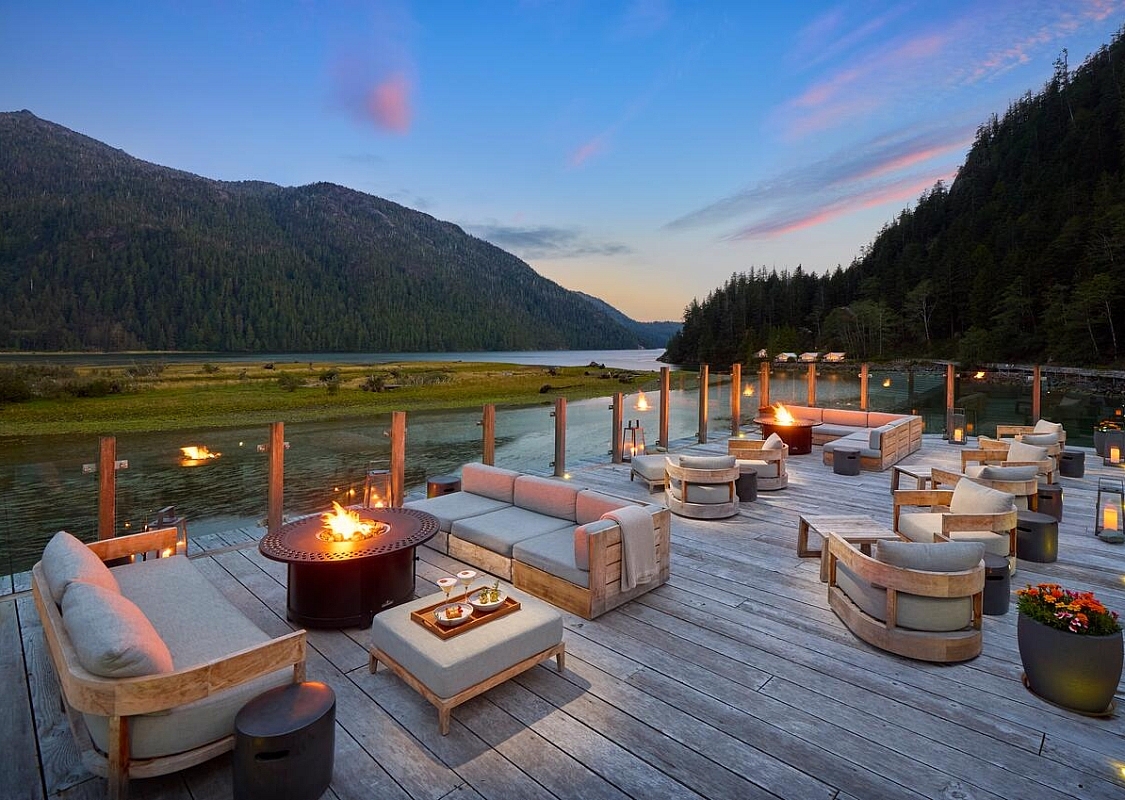Sitzgelegenheiten und Feuerstellen auf einer Holzterrasse mit Blick auf eine Bucht.