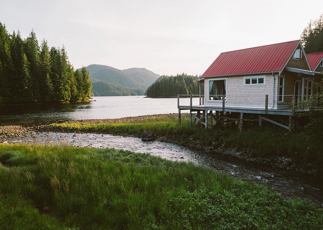 Zwei Lodge-Gebäude stehen auf einer erhöhten Plattform am Ufer einer Bucht.