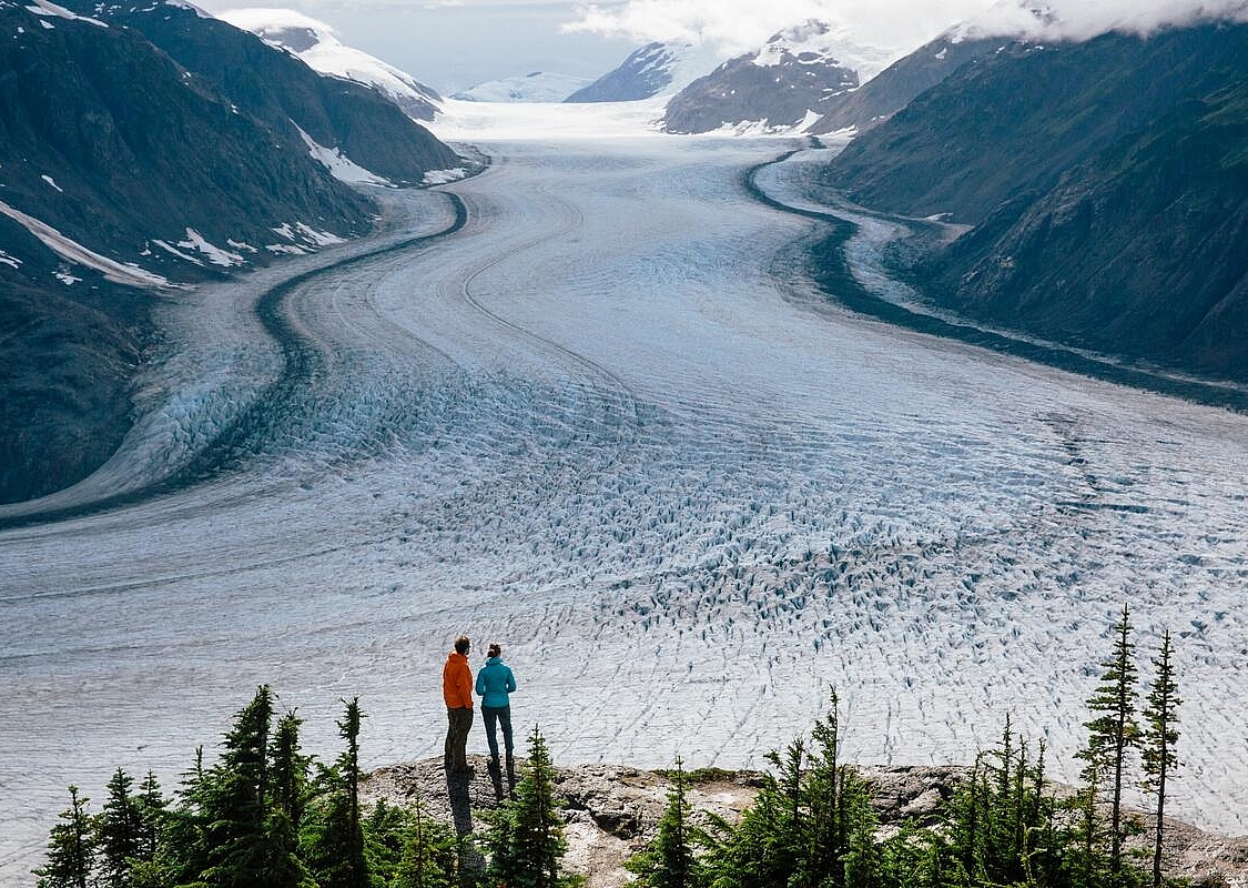 Zwei Personen stehen auf einem Felsvorsprung mit Blick auf einen riesigen Gletscher.