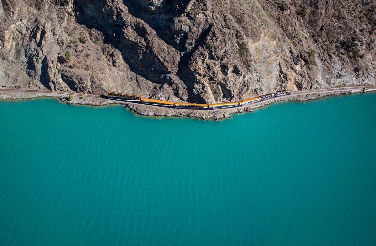 A train makes its way along the banks of a turquoise-coloured lake.