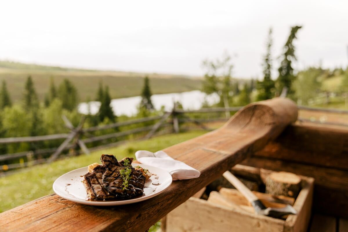 A plate of food sits on a wooden railing looking out over a lake.