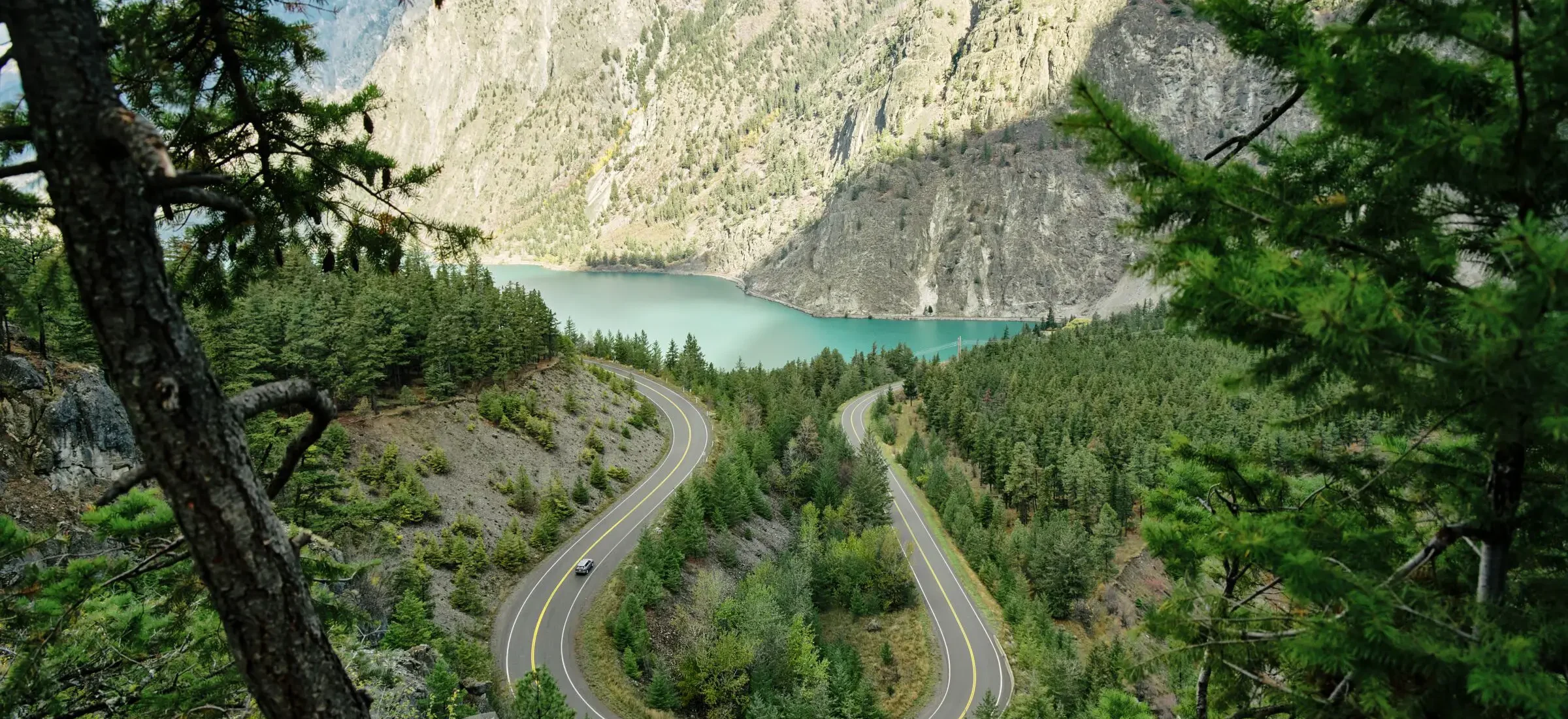 View toward a turquoise lake with a forested landscape in the foreground and sagebrush-covered mountains in the background.