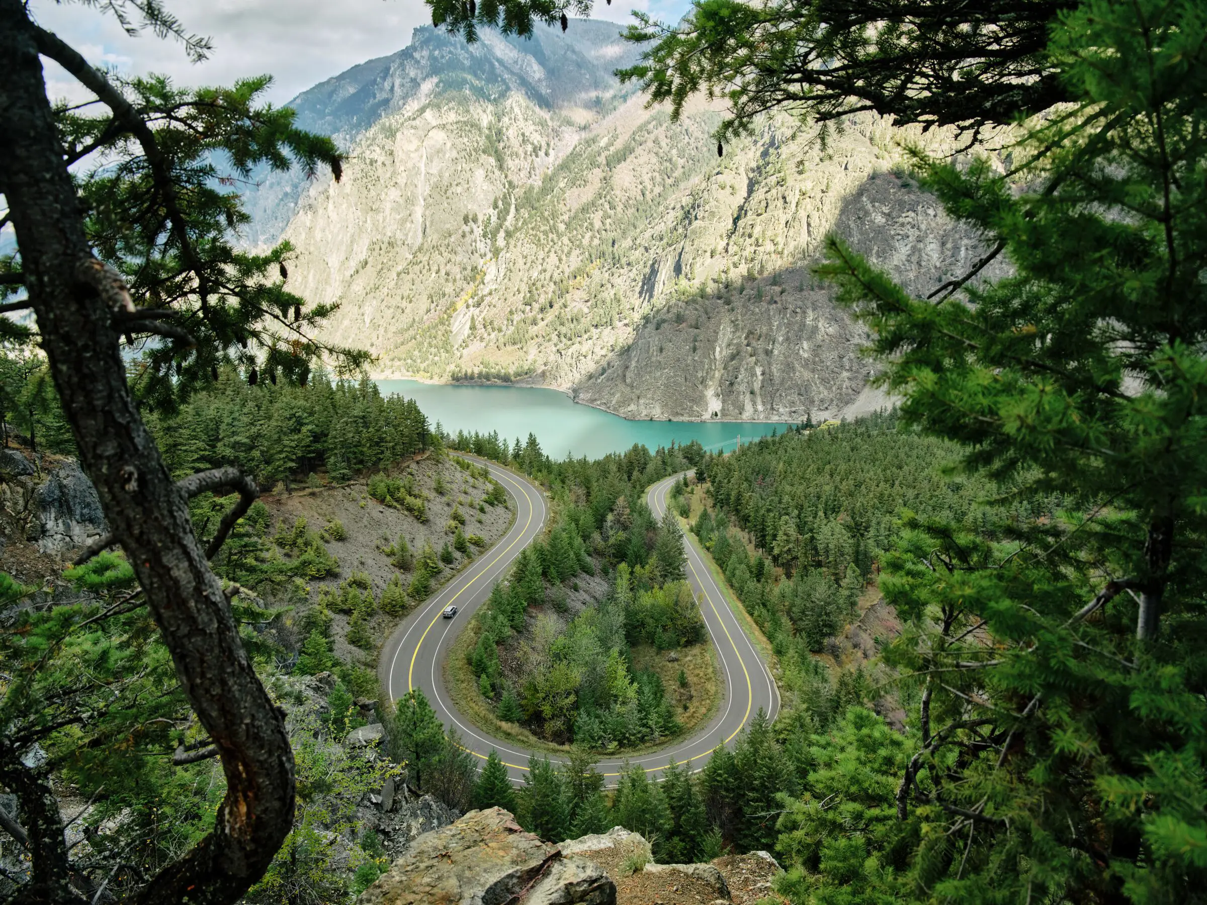 Blick auf einen türkisfarbenen See mit einer bewaldeten Landschaft im Vordergrund und mit Salbeibusch bewachsenen Bergen im Hintergrund.