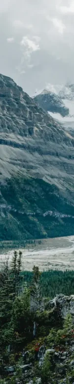 A hiker is perched on a trail. In the background is Berg Lake and Mt Robson.