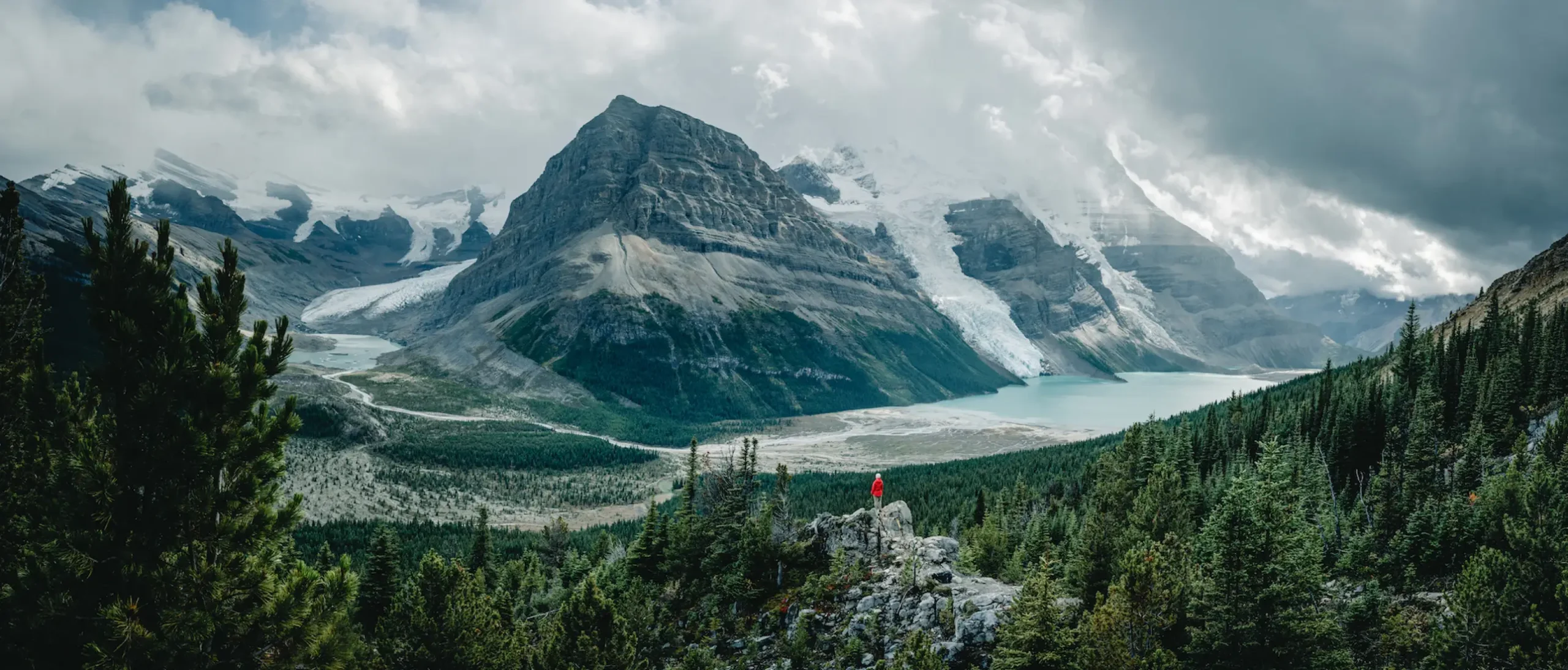 Ein*e Wander*in sitzt auf einem Wanderweg. Im Hintergrund sind der Berg Lake und der Mt Robson zu sehen.