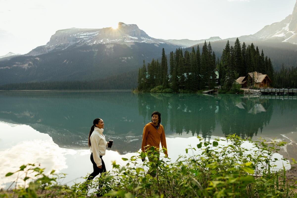 Dos amigos paseando por la orilla del lago Emerald, en el Parque Nacional Yoho, en las Montañas Rocosas canadienses, con el Emerald Lake Lodge al fondo.