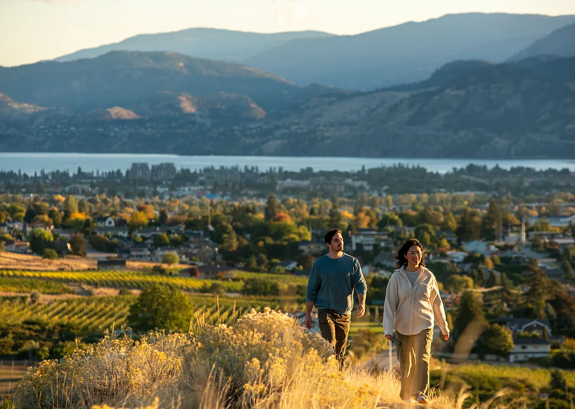 Ein Paar beim Wandern am Munson Mountain, im Hintergrund Penticton und der Okanagan-See.