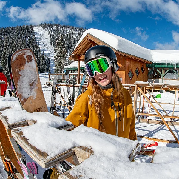A skier standing happily by the ski racks outside the main lodge at Whitewater Mountain Resort in Nelson.