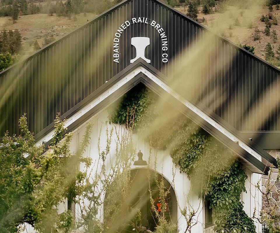 Exterior view of Abandoned Rail Brewing Co. in Penticton, with the brewery entrance framed by greenery and hillside scenery.