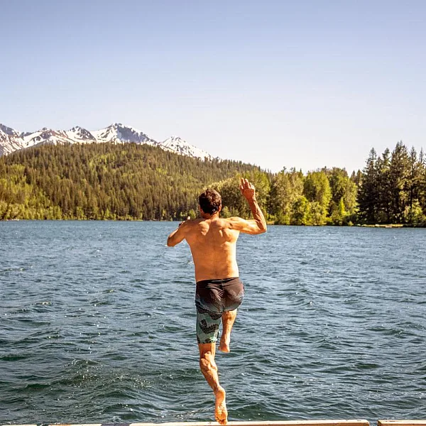 A guest jumping off the dock into the lake at Tyax Lodge, a wilderness lodge near Gold Bridge, with the forest and mountains in the background.