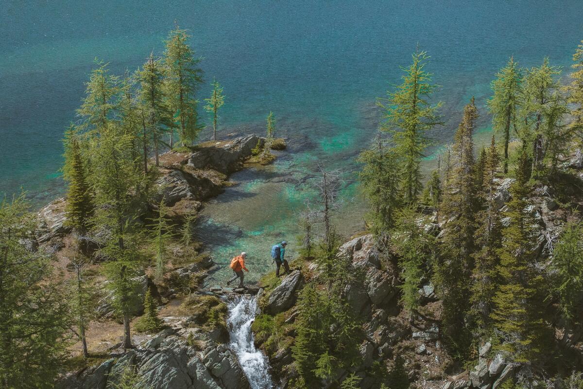 Dos amigos haciendo senderismo junto a un lago glaciar de color turquesa en los Bugaboos durante una excursión de senderismo con traslado en helicóptero organizada por CMH Bugaboos.